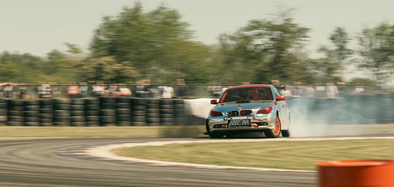 A chrome-wrapped BMW smoking through the corner in front of the tyre wall