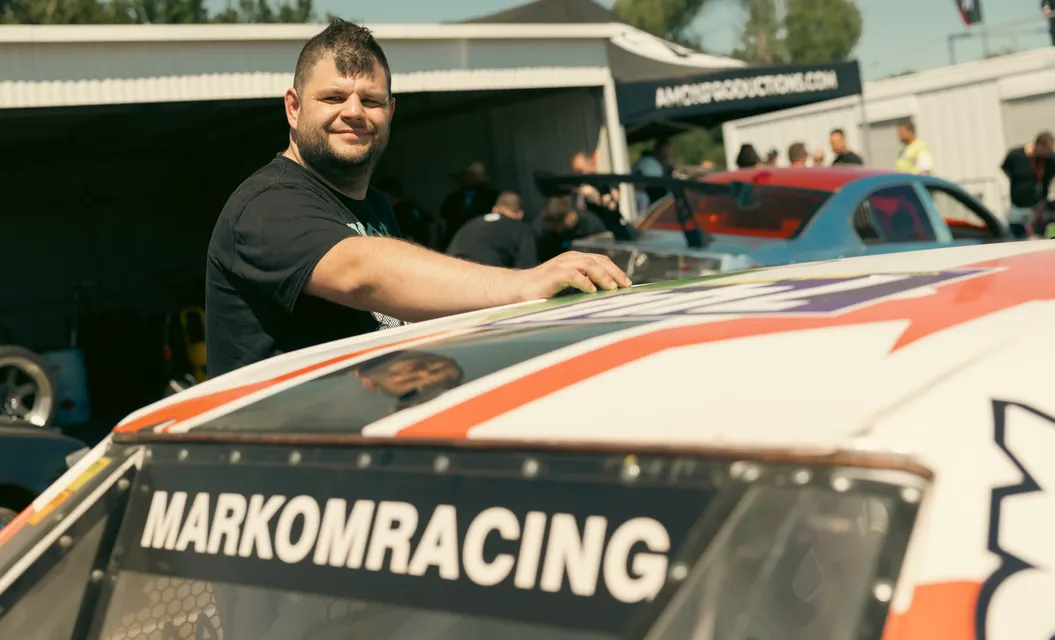 A smiling team member behind the Markom Racing race car