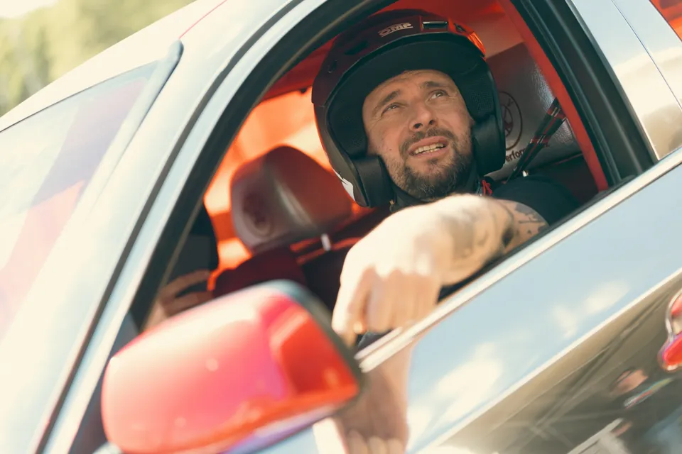 A driver in a helmet leans out of the car window