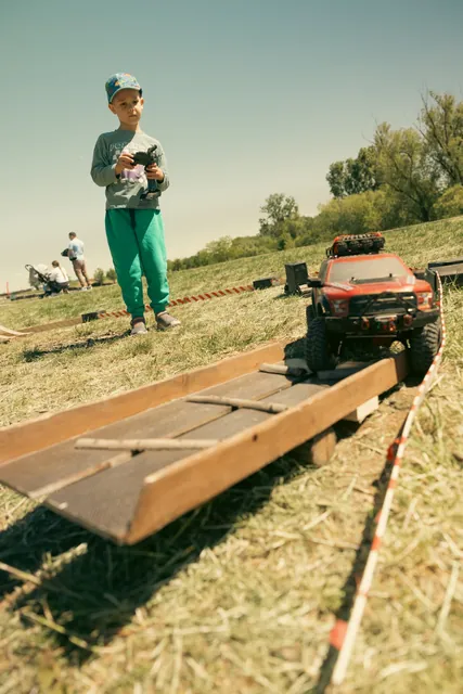 A boy drives a remote-controlled off-road car on a wooden obstacle course
