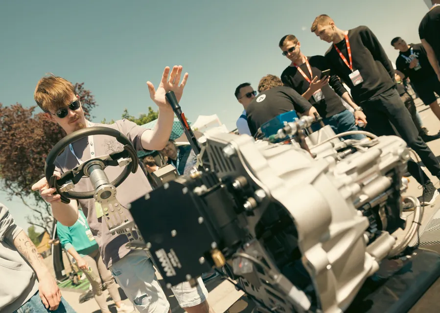 A visitor holding a steering wheel next to an exhibited gearbox