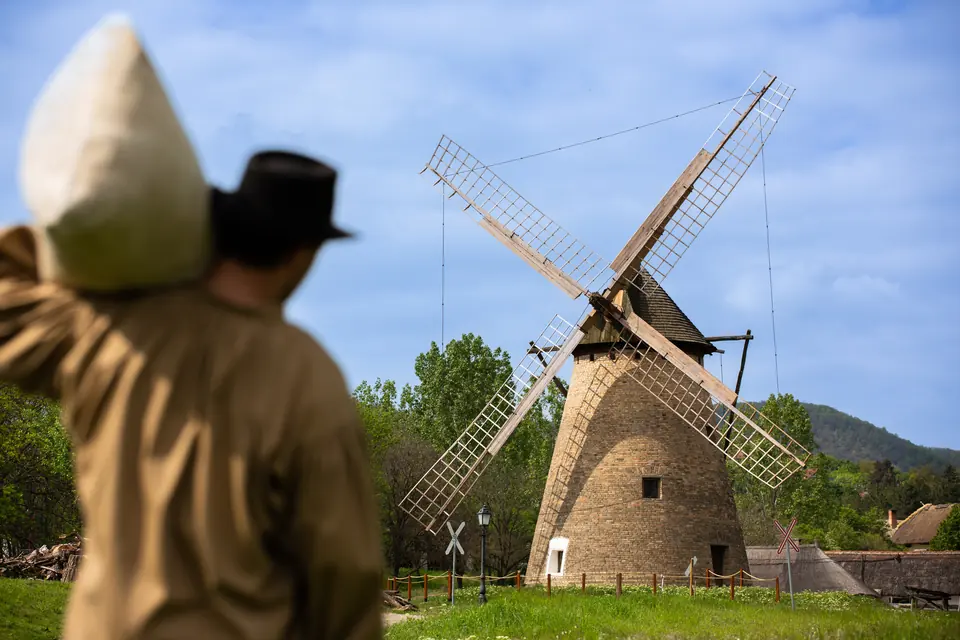 Szélmalom egy szabadtéri múzeumban, előtérben egy zsákot cipelő szereplővel