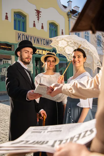Korhű jelmezes szereplők újsággal egy múzeumi utcán