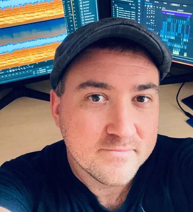 Dávid Egerváry taking a selfie in the edit suite, with audio and video editing software on two monitors behind him