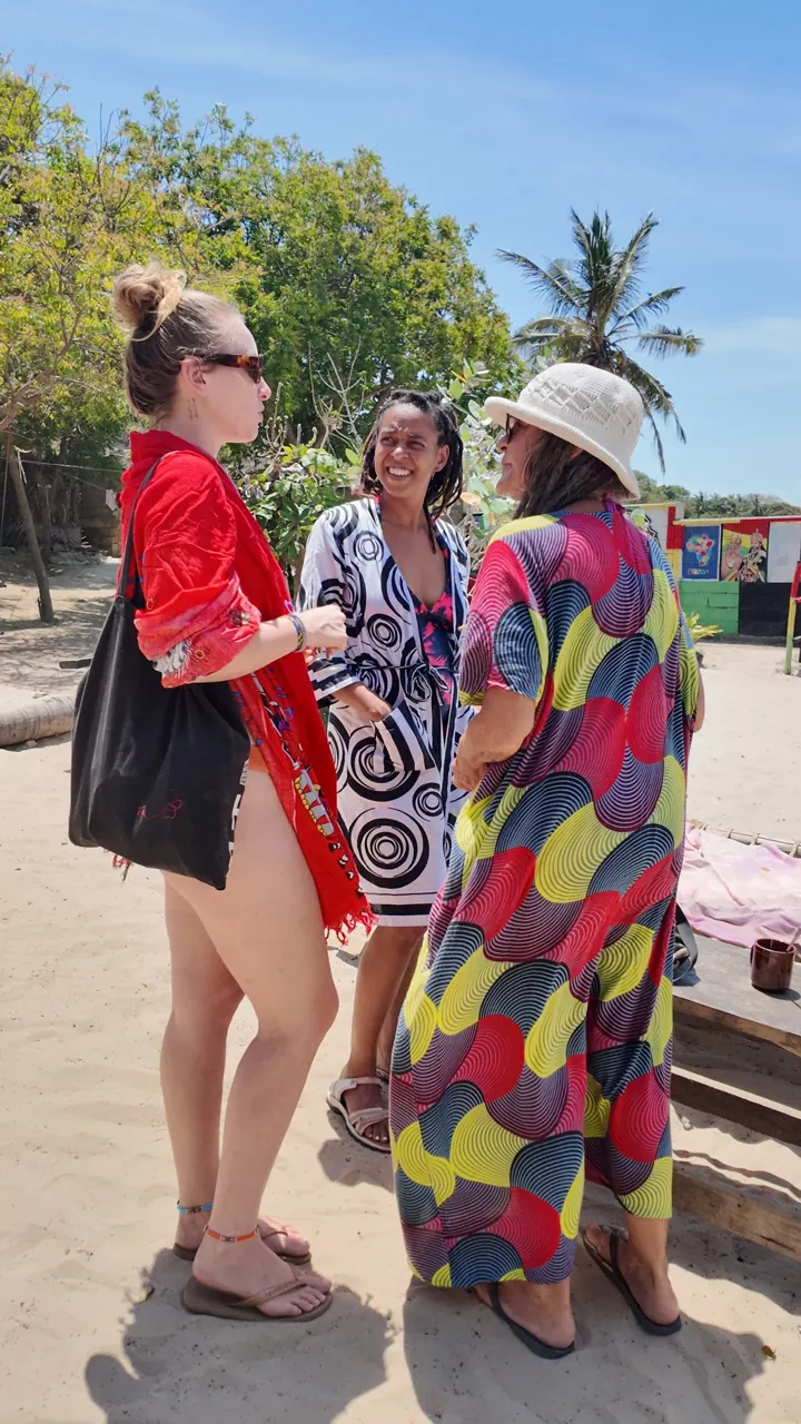 Fatime chatting with two women on the sandy beach, in colourful clothes