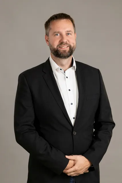 Üzleti portréfotó szürke stúdióháttér előtt, sötét zakóban, fehér ingben